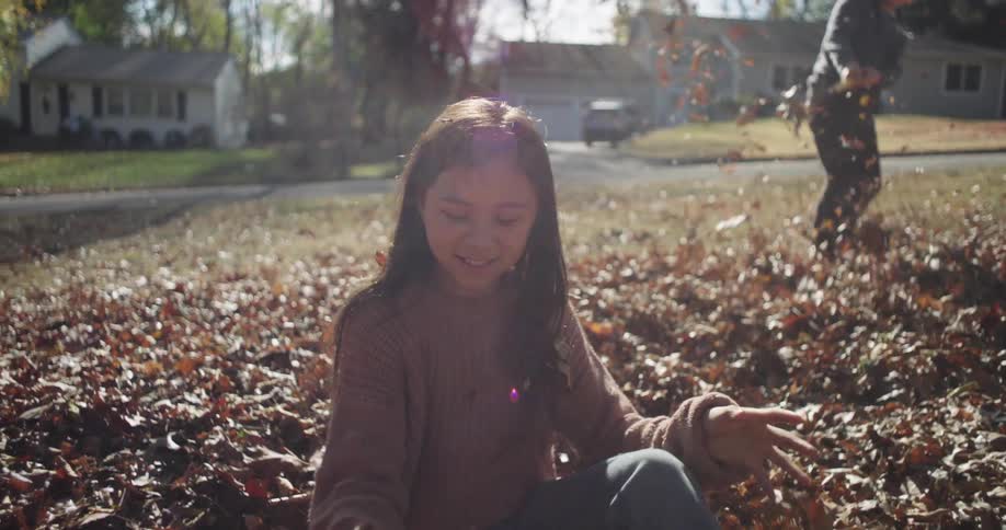 Girl sitting in a pile of leaves happily tossing them in the air