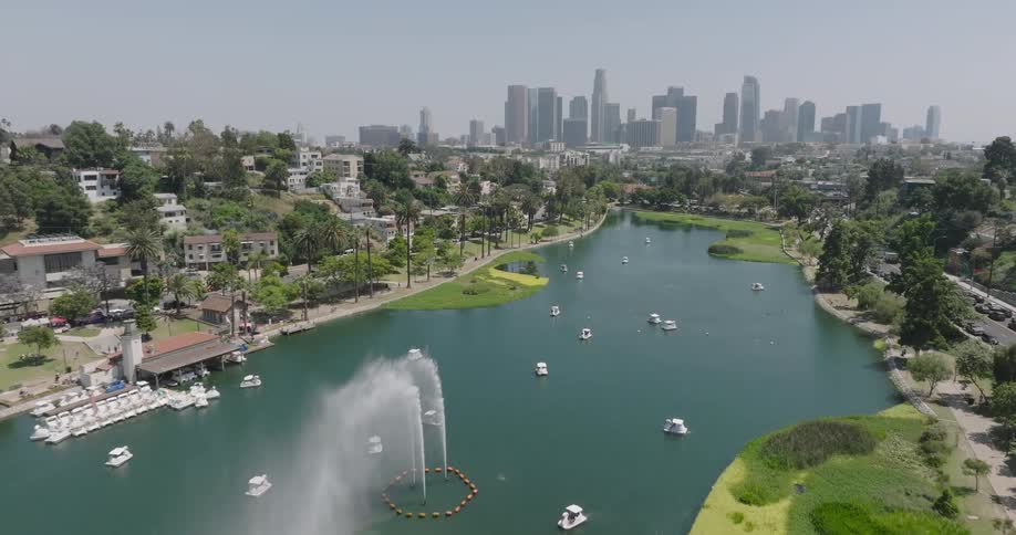 An aerial view of echo park lake in los angeles with its iconic swan boats a fountain and the city skyline in the distance