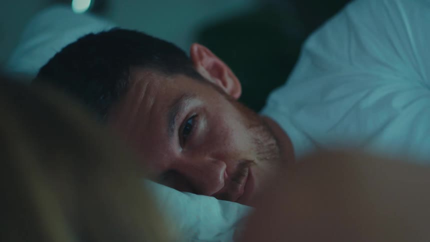A blonde woman and a man lie in bed looking at each other with love in the bedroom