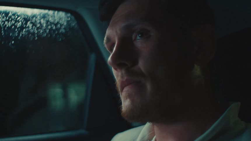 A pensive man sitting in a car at nighttalks to the driver near a rainspeckled window illuminated by soft moody lighting