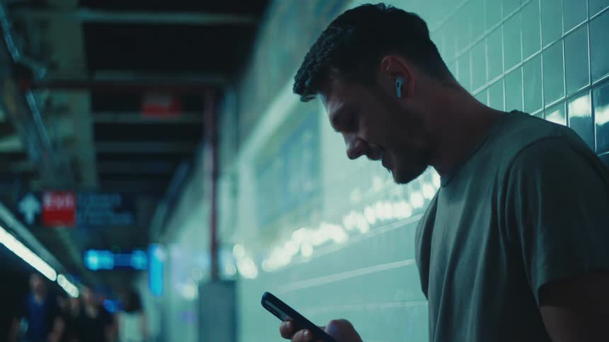 Man at a subway station laughs while using his phone with people walking by