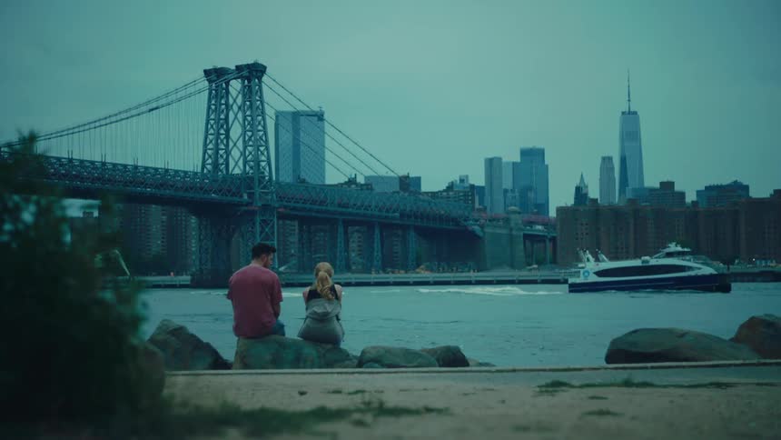 Woman and a man sitting on the seashore with a metropolis on the horizon