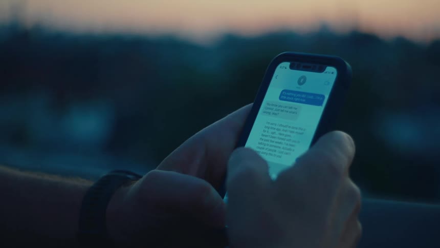 A person holding a smartphone and typing a message against the city skyline at sunset
