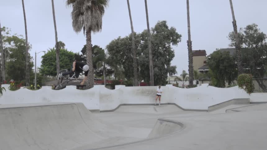 People in a park, one person does a jump on their bike