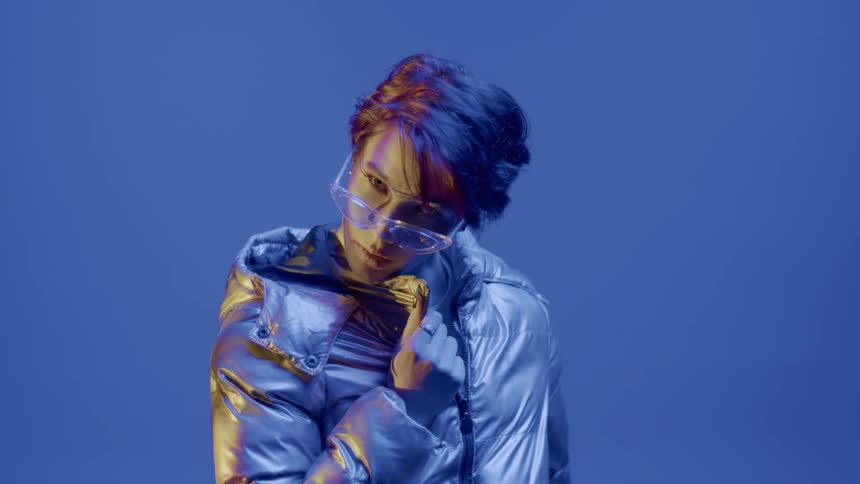 Woman in a silver jacket and glasses modeling indoors with purple light
