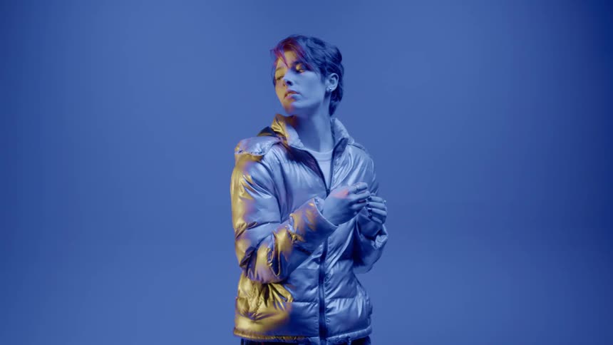 Woman indoors in a long jacket against a blue background