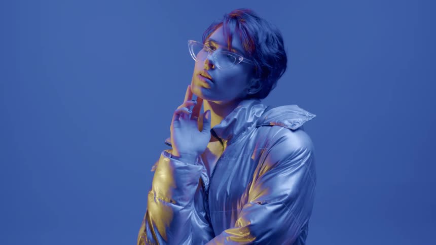 Female model moves through poses while modeling eyeglasses and a coat against a blue background