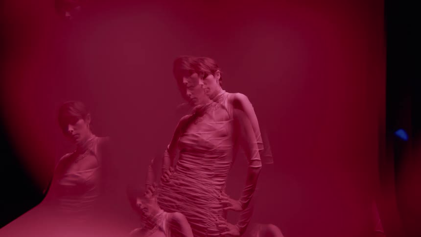 Blonde woman in dress in multiple exposures in an indoor space with a pink background
