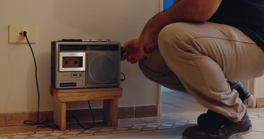 A man is turning on a vintage cassette player resting on a wooden stool