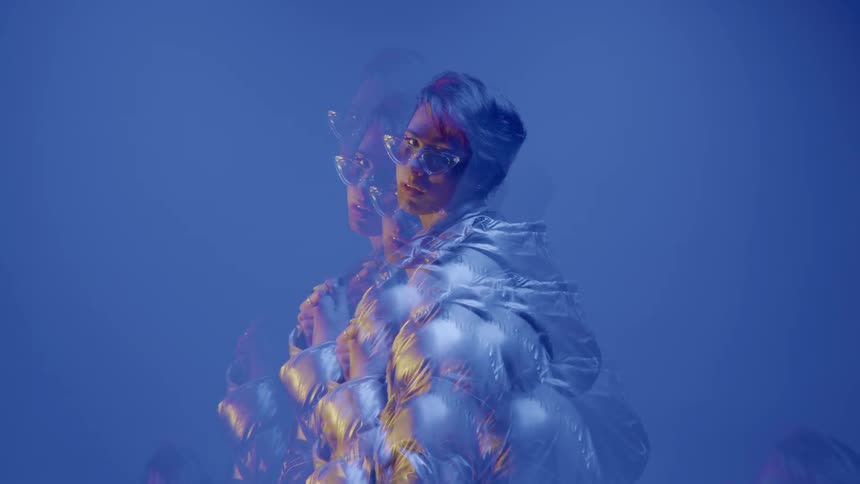 A person is wearing a futuristic reflective and metallic outfit with a distorted multiexposure effect against a blue background