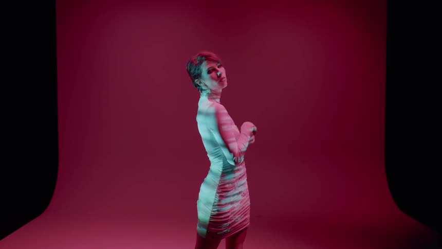 Woman in a long sleeve white dress modeling while standing in an indoor space with a pink backdrop