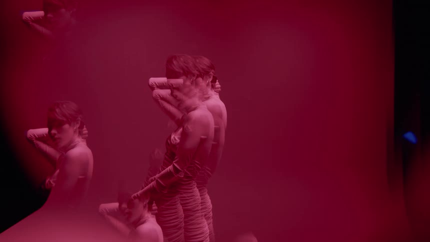 Woman in white dress in multiple exposures in an indoor space against a red background