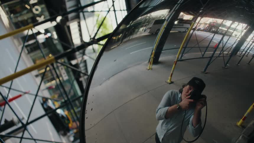 A man in a cap with a camera on his face approaching a mirror and taking a picture of his reflection
