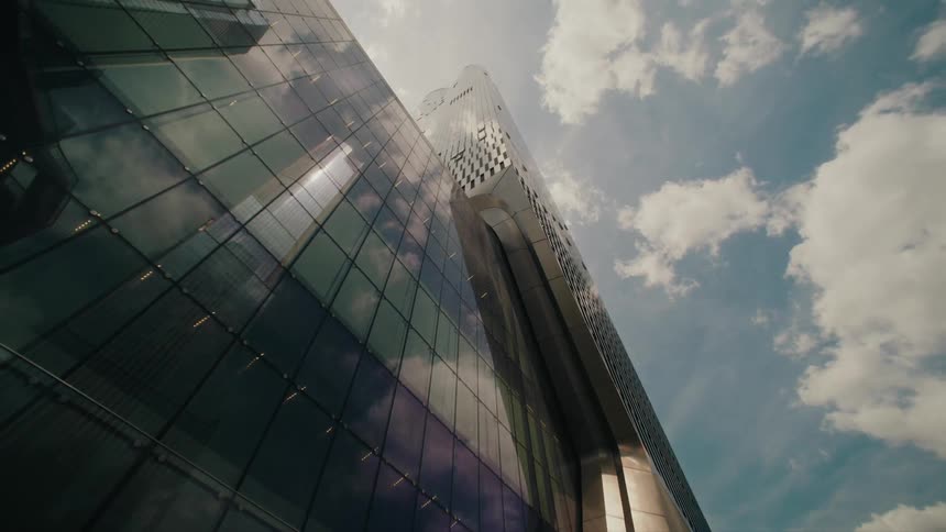 Clouds float over a tall glass skyscraper in a city