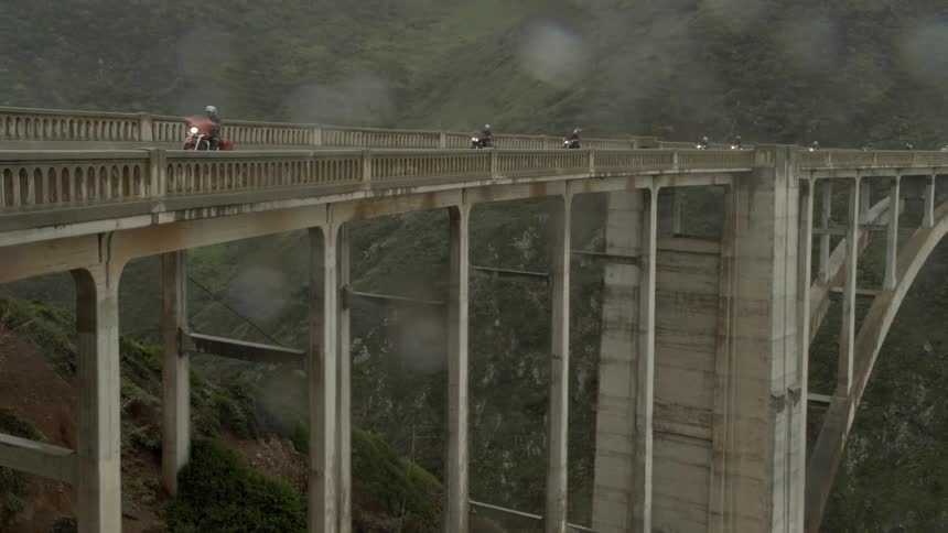 A group of motorcyclists riding over a bridge in the country