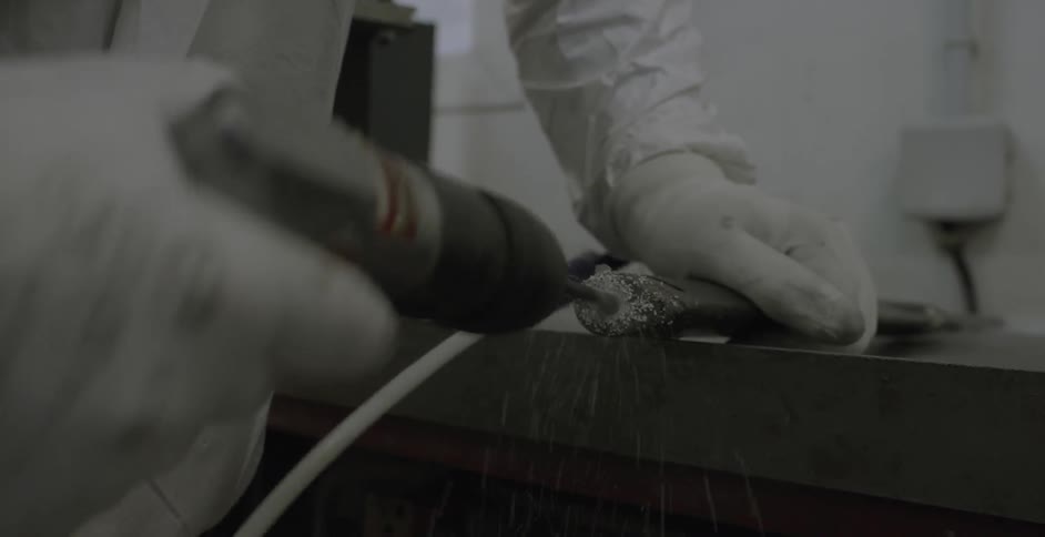 A person uses a drill to bore out a hole in some kind of stick