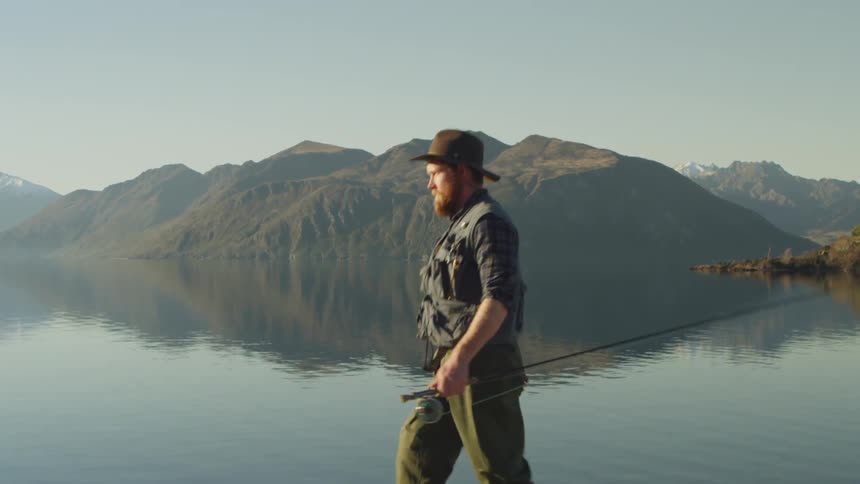 Man walking with a fishing pole beside a lake on a cloudy day