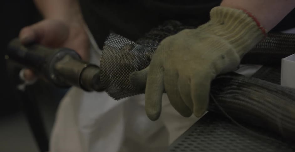 A person wearing gloves in molding wire mesh around something and holding a piece of equipment in his other hand