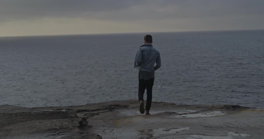 Man walking to the edge of a cliff with water ahead then throws something