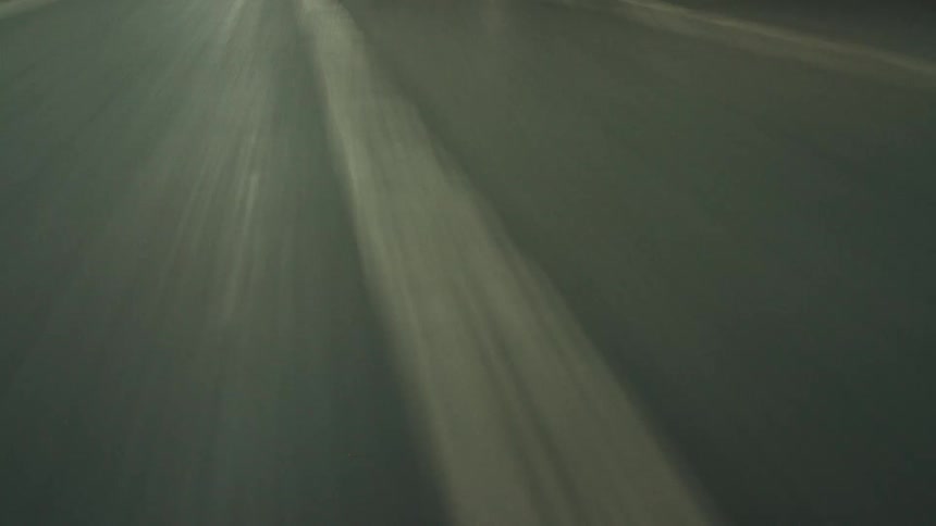 A low angle shot shows the perspective from a vehicle driving through a dimly lit underground parking garage