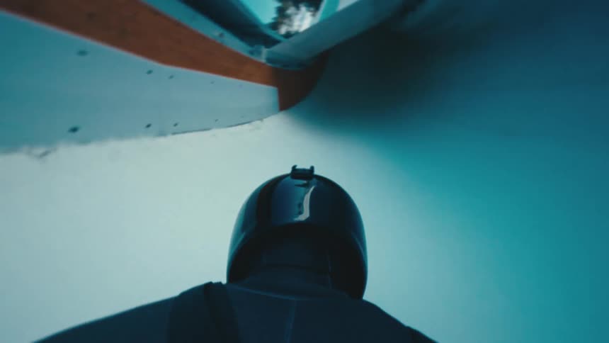 A bobsledder speeds down the track transitioning between open and closed tunnels emphasizing dynamic motion and intensity