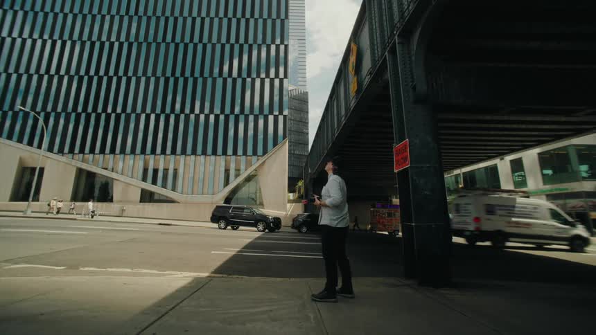 Man holding a camera while standing next to an overpass and a street in a metropolis with vehicle traffic