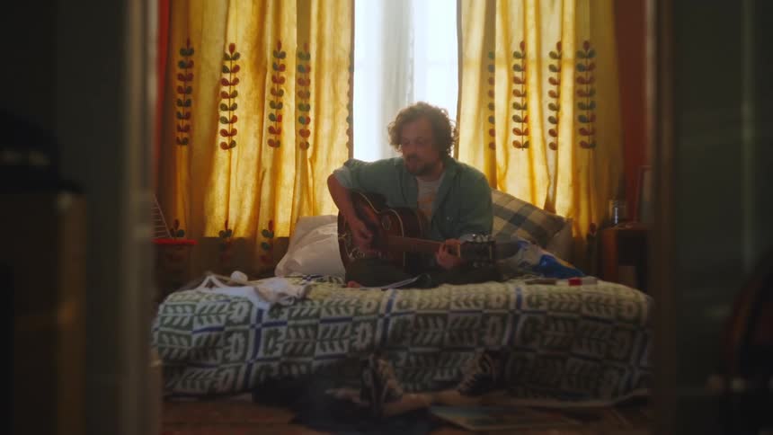 Man sitting on his bed playing guitar singing and writing music