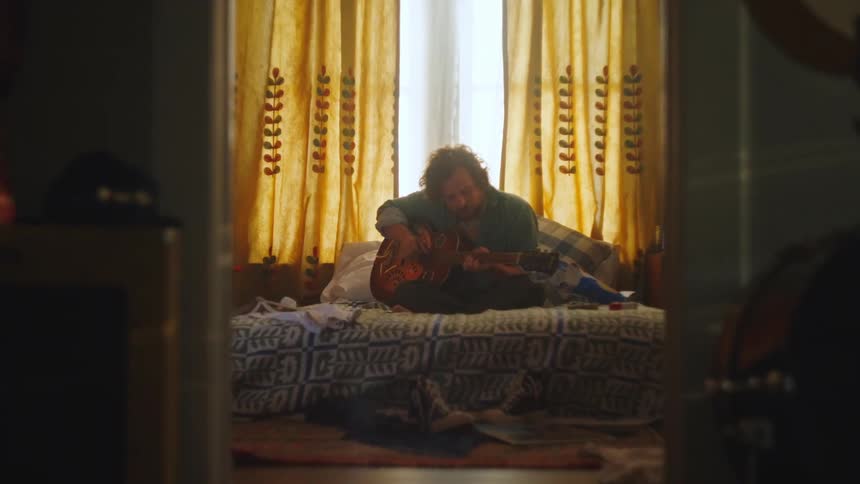 Lying man sits up in bed and starts playing guitar
