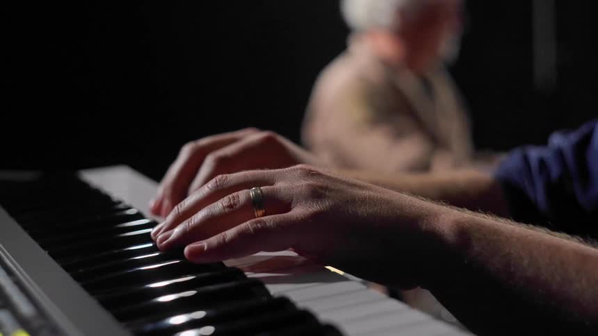 One person plays the piano while another plays the drums with his hands