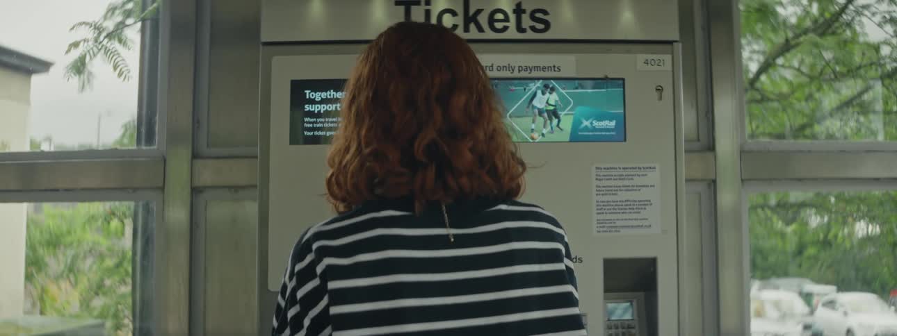 Back of red haired female buying tickets from a ticket kiosk