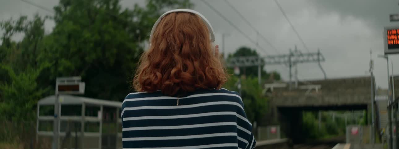 Redheaded woman outdoors with headphones near a train station
