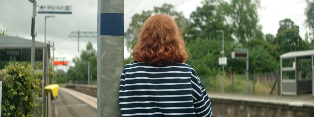 Woman leaning on metal column waiting for the train at rural outdoor station