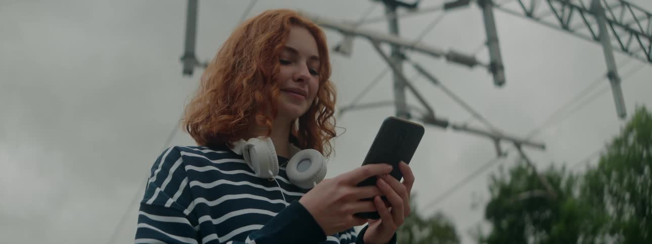 Redheaded woman standing in an outdoor area interacting with a smartphone