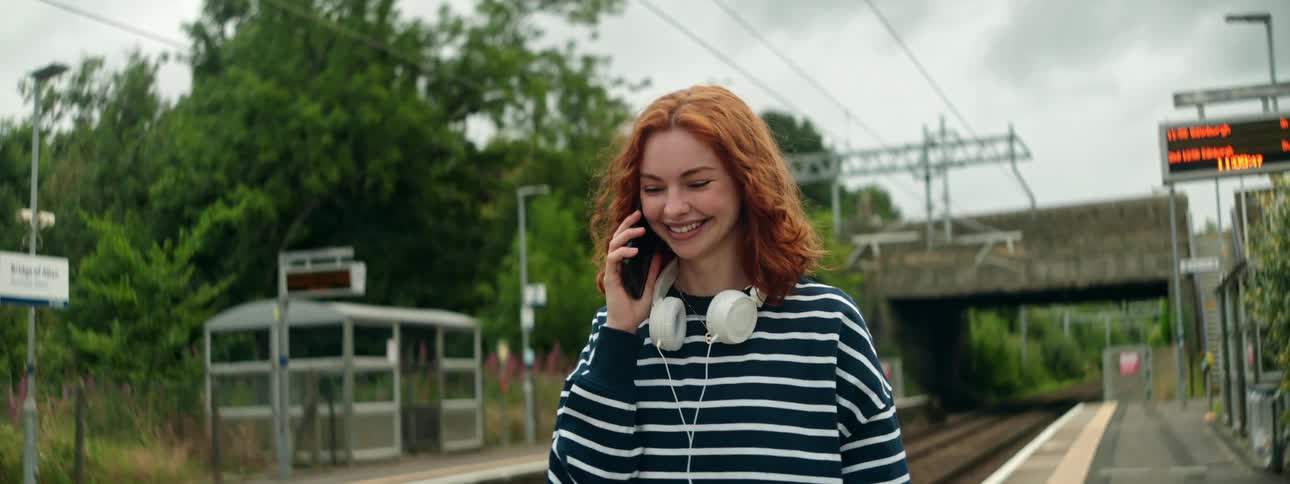 A footage of a lady making a phone call while walking by the rail side
