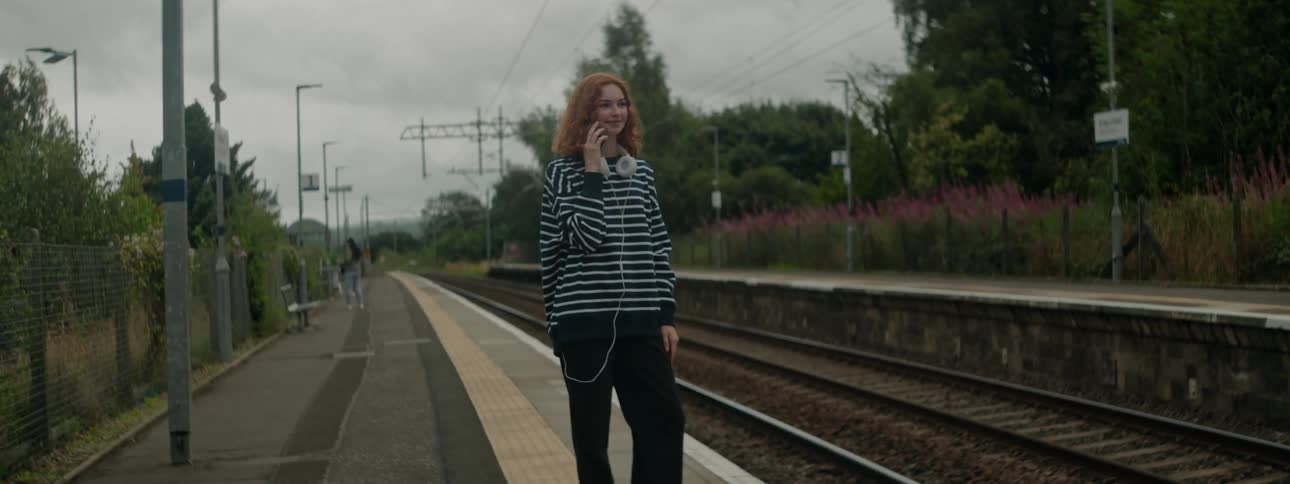 A clip of a lady waiting and making a call by the rail track
