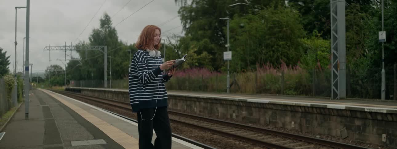 Woman next to a train track in a subway station reading a book