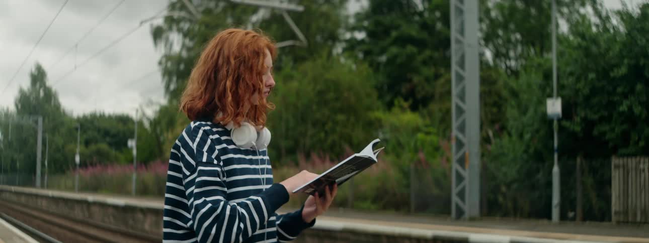 A clip of a lady standing and reading by the rail side