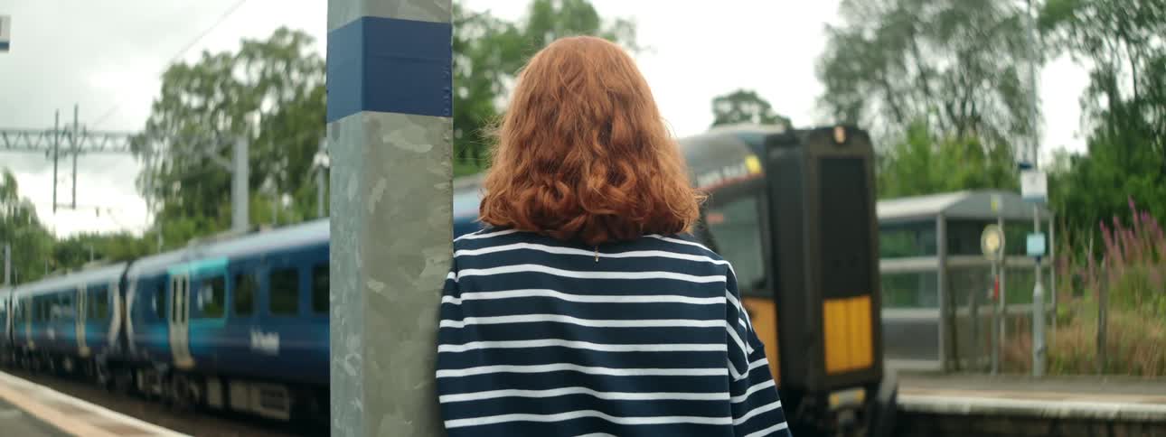 Woman leaning on metal column at train station watching metro go by