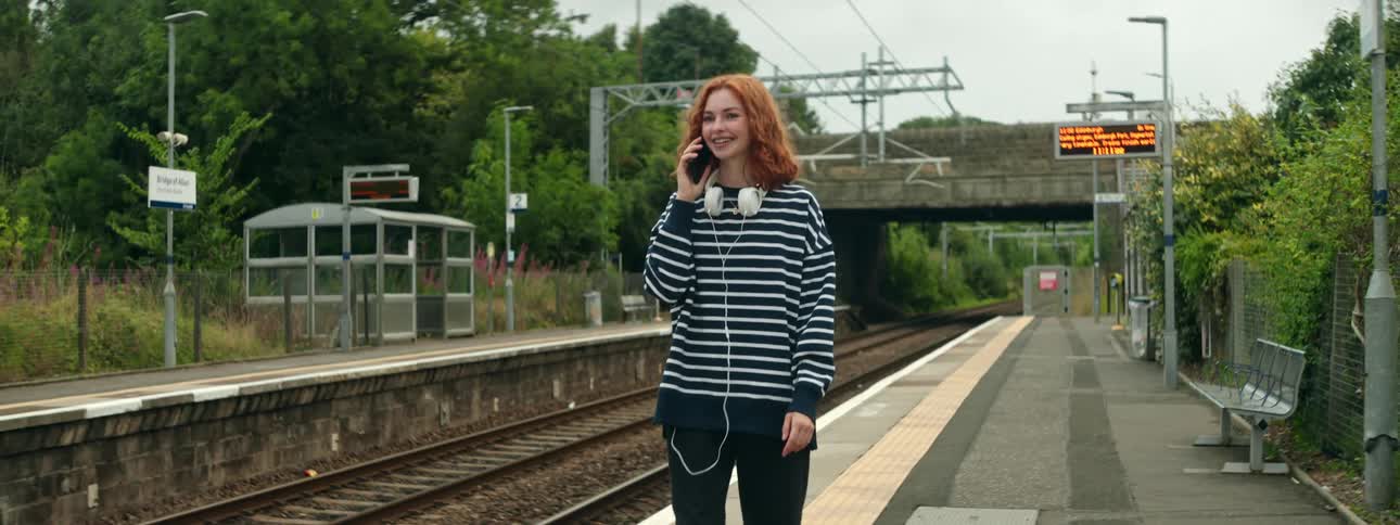 Woman walking in the sea outside next to a train track talking on her cell phone