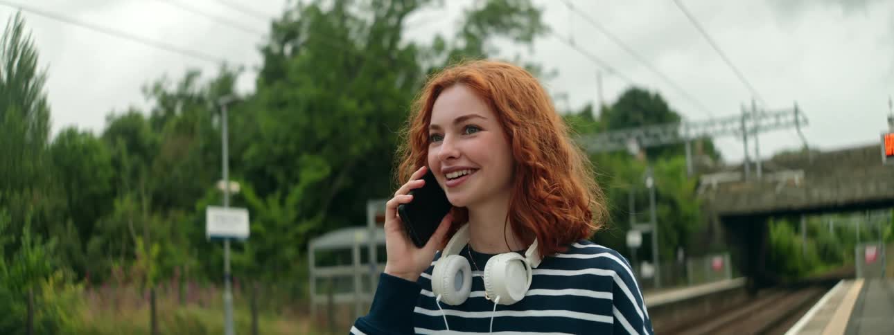 Portrait of a redhaired woman walking next to a train station on a phone call