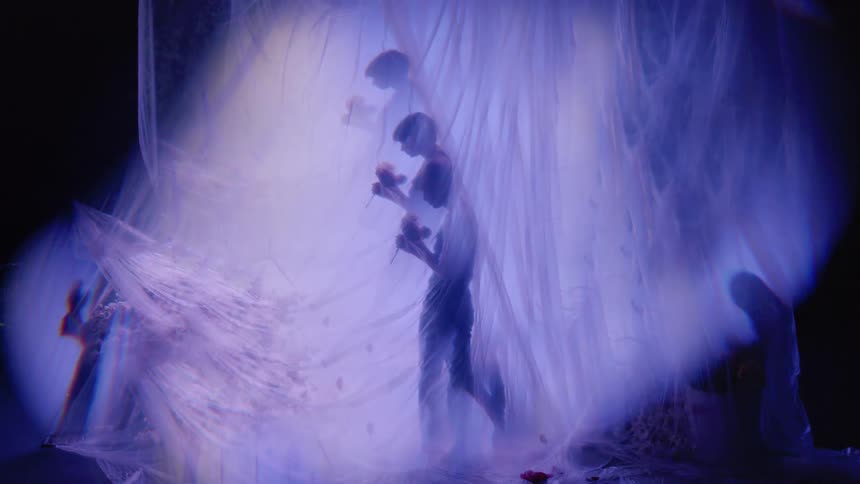 Multiple exposures of a woman performing behind a purple light curtain
