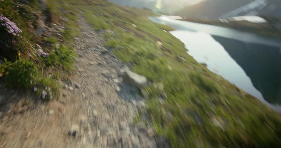 Moving point of view along a trail along the edge of a lake with mountains around it