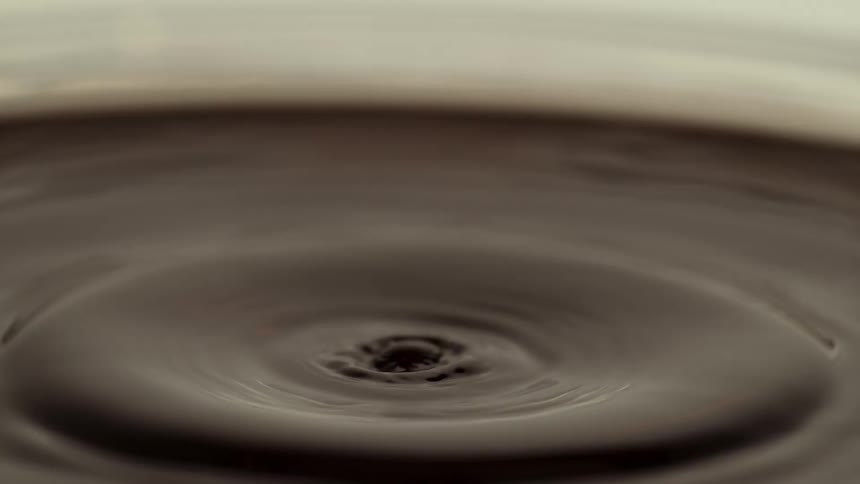 A single drop of coffee falls into a cup of coffee