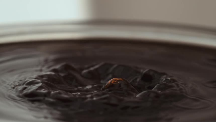 Droplets of dark liquid splash into a pool creating a crown of ripples