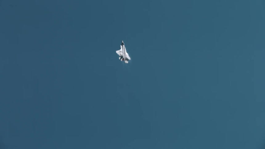 A fighter jet flies high in a clear blue sky leaving thin white contrails