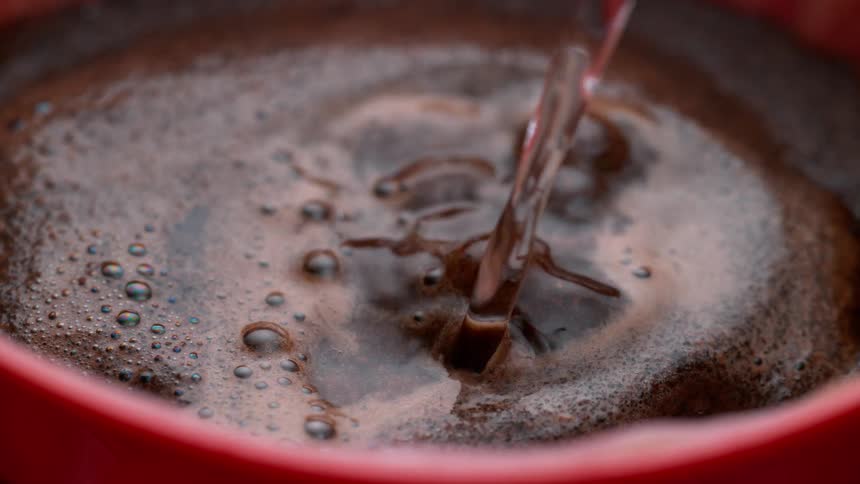 Boiling water is poured into a cup with coffee