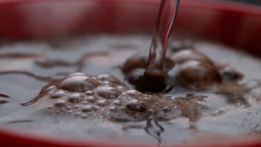 Water being poured into a red mug containing coffee grounds creating bubbles and foam
