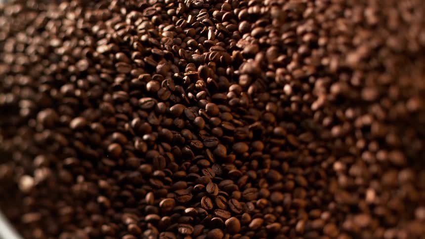 Roasted coffee beans slowly slide down the side of a container