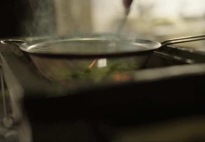 A hand stirring food in a pan over an open flame with steam rising creating a warm and focused cooking scene