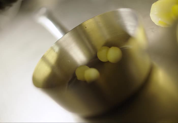 Small white balls of a potato being dumped onto a metal surface